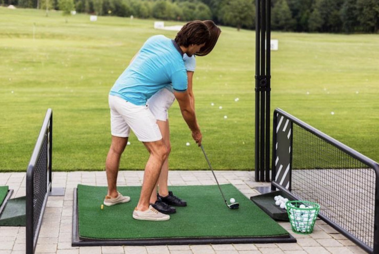 Golfer practicing swing with coach on driving range mat